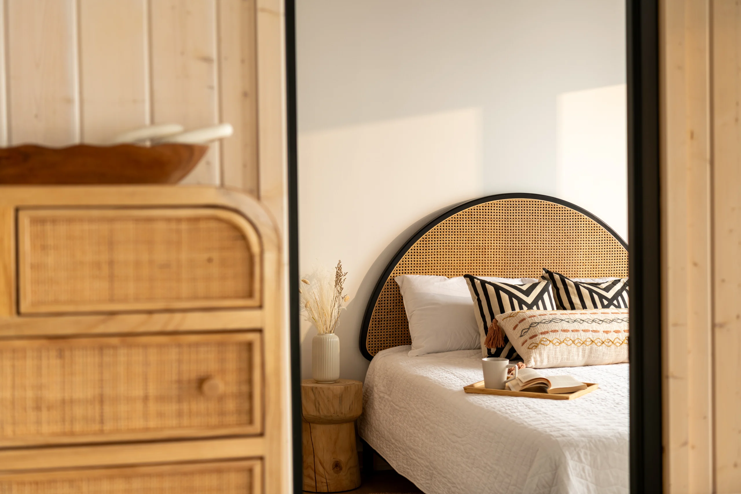 Interior Design - A cozy bedroom featuring a rattan headboard, decorative pillows, and a bedside table with a book and a cup. Dexign Matter Studio