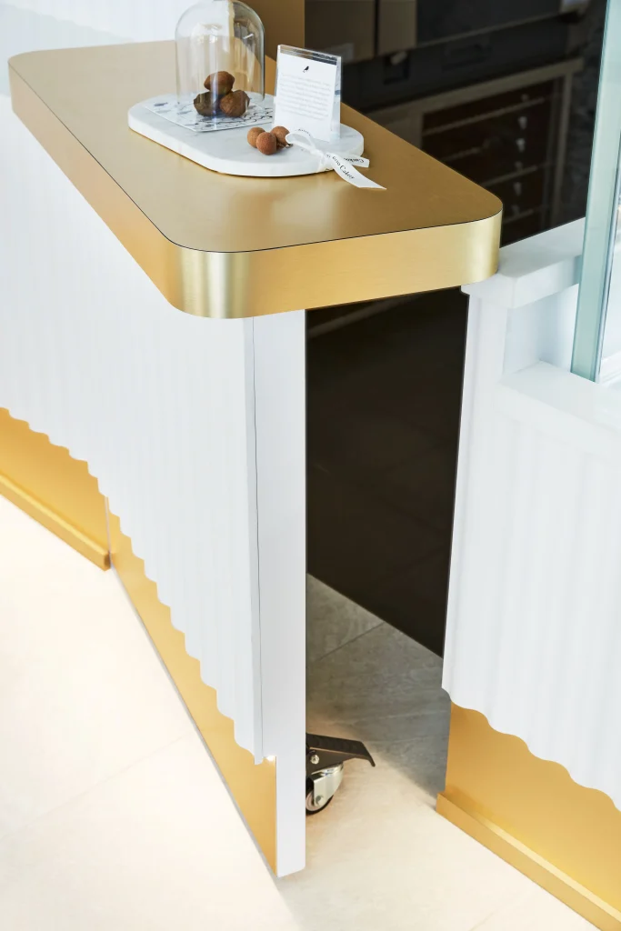 Interior Design - Reception desk featuring a gold top and white ribbed design with a decorative item on top. Dexign Matter Studio