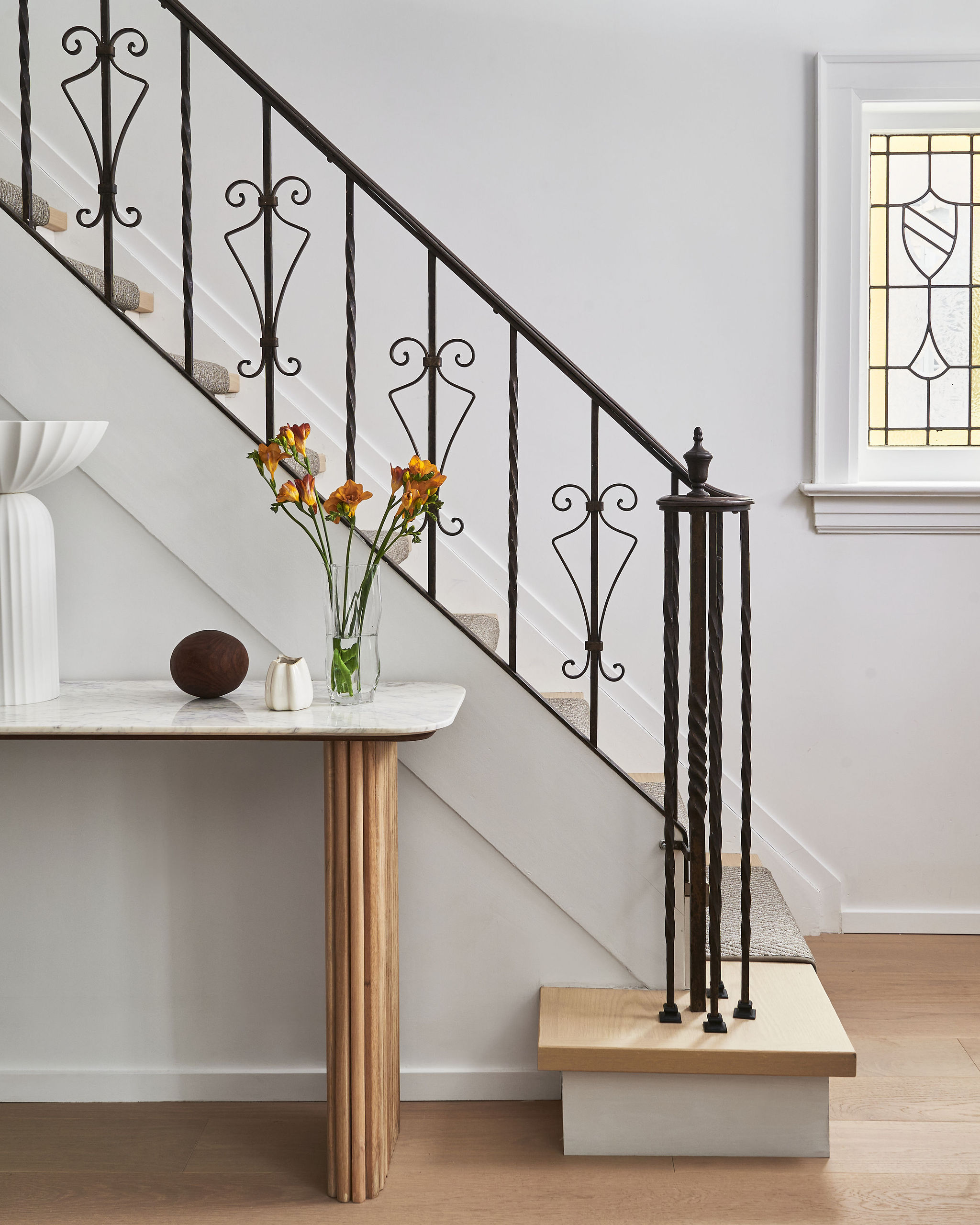 Interior Design - Staircase featuring an ornate black railing and a vase of flowers on a table. Dexign Matter Studio