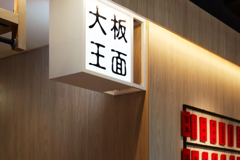Interior Design - Illuminated sign with Chinese characters for a noodle restaurant displayed on a wooden wall. Dexign Matter Studio