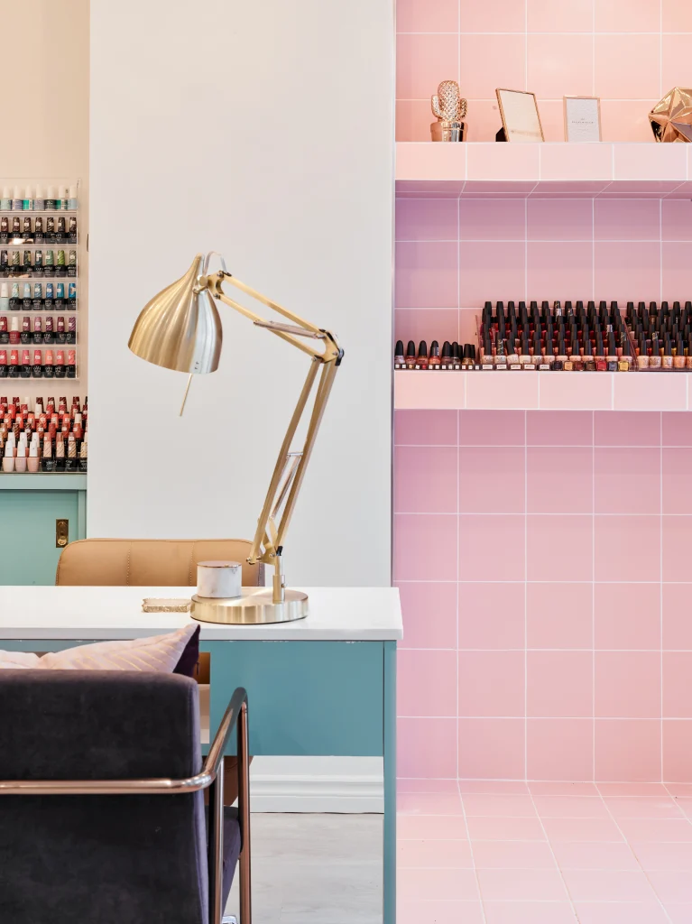 Interior Design - A modern nail salon workspace featuring a desk with a lamp and shelves of nail polish. Dexign Matter Studio