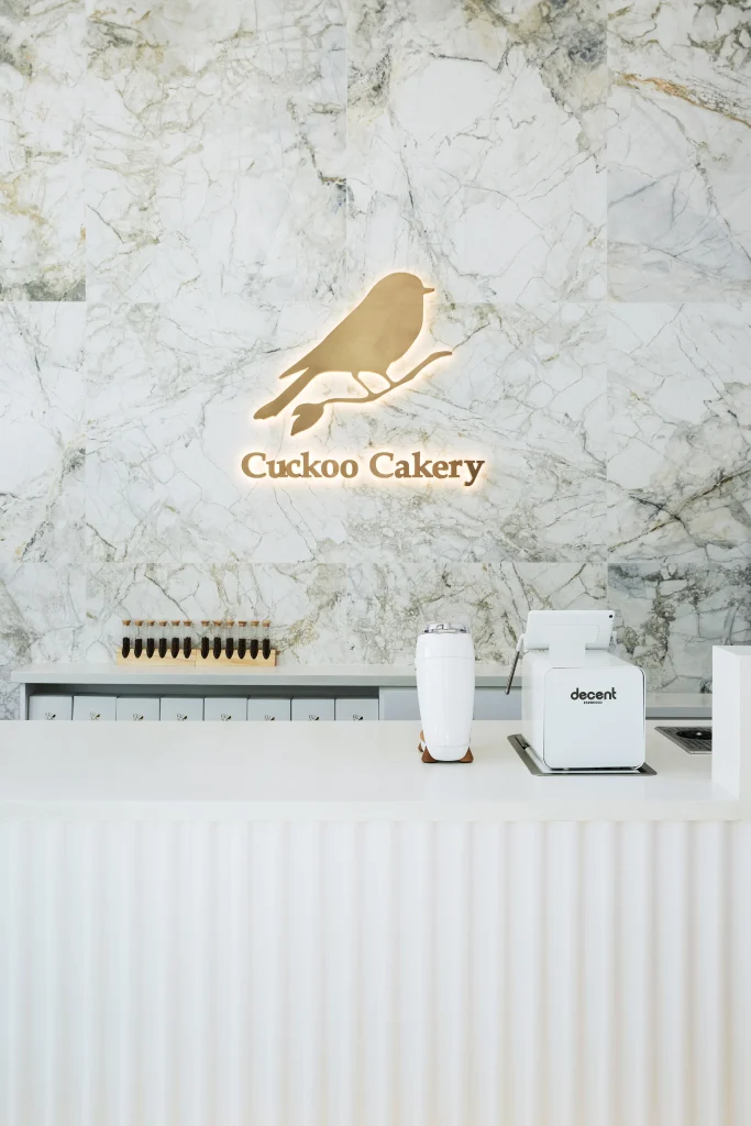 Interior Design - Interior view of Cuckoo Cakery featuring a marble wall and a decorative bird logo. Dexign Matter Studio