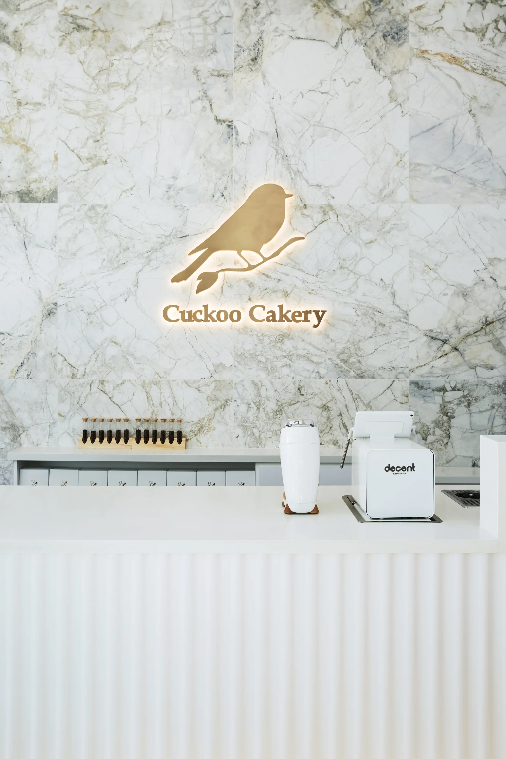Interior Design - Interior view of Cuckoo Cakery featuring a marble wall and a decorative bird logo. Dexign Matter Studio