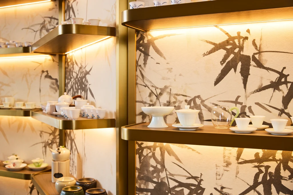 Interior Design - A collection of tea sets displayed on shelves with bamboo-themed wallpaper and warm lighting. Dexign Matter Studio