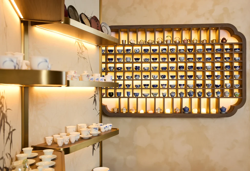 Interior Design - A collection of tea ware displayed on shelves with warm lighting in a modern interior. Dexign Matter Studio