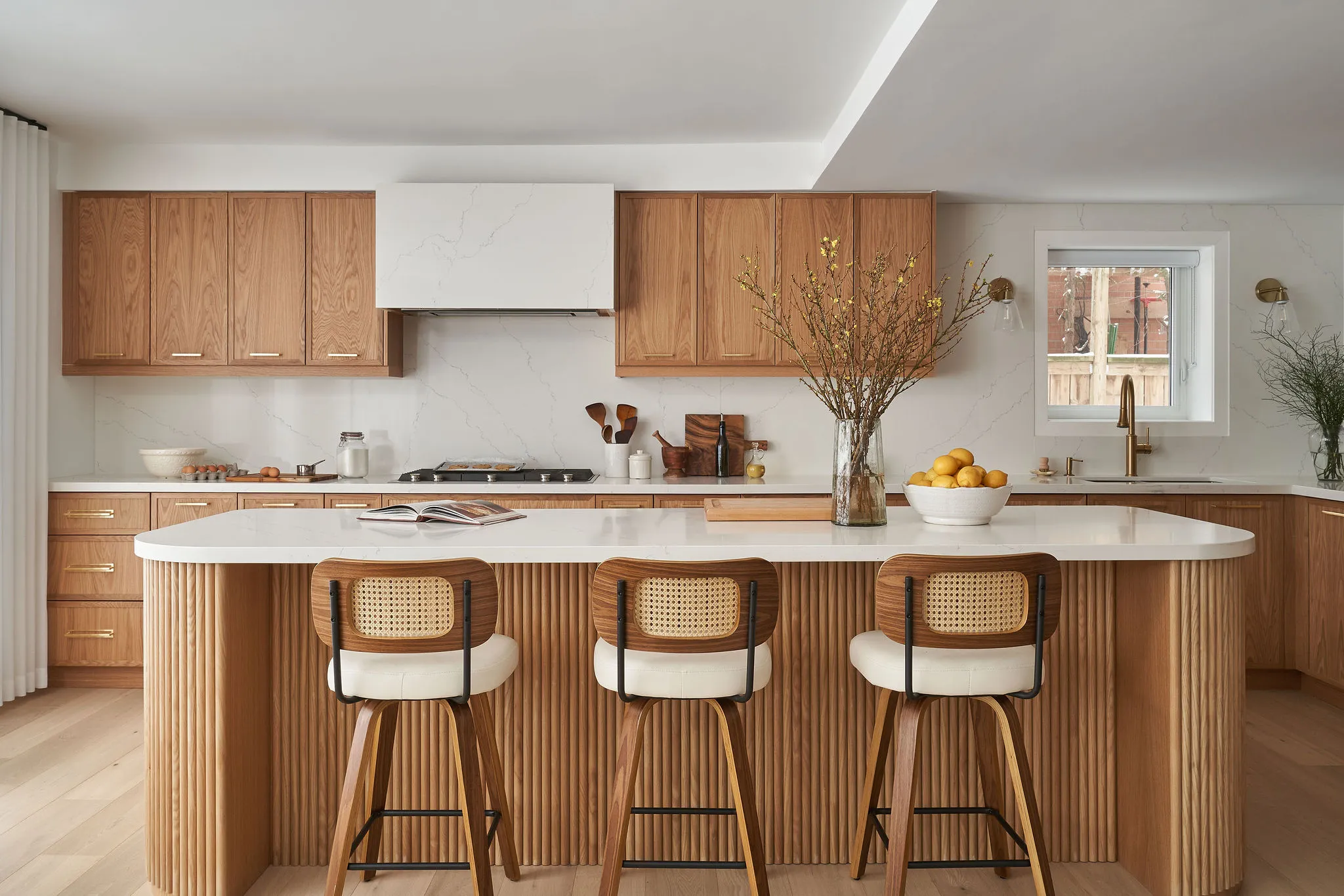Interior Design - Contemporary kitchen featuring wooden cabinets, a white countertop, and bar stools with a decorative vase. Dexign Matter Studio