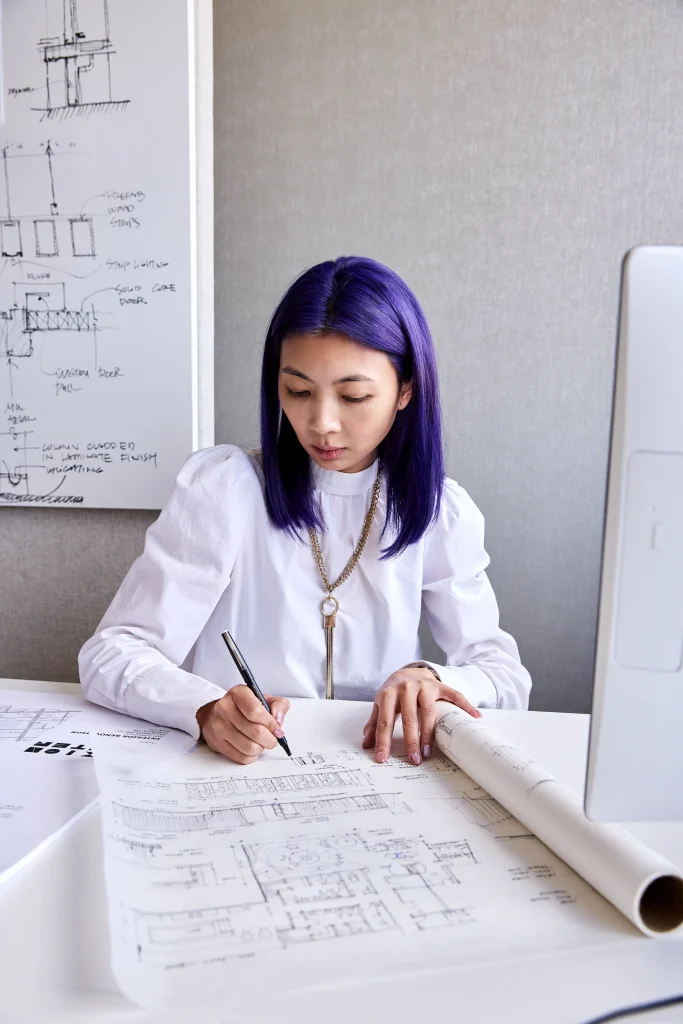 Interior Design - Interior designer with blue hair sketching plans on paper at a desk with a computer and sketches in the background. Dexign Matter Studio