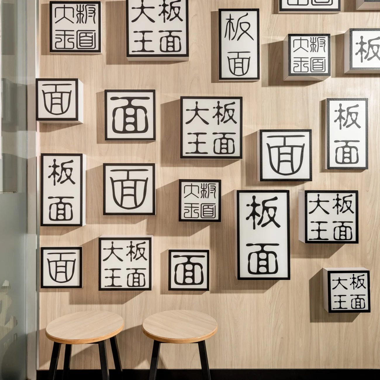 Interior Design - Wall featuring decorative boxes with Chinese characters and two wooden stools in front. Dexign Matter Studio
