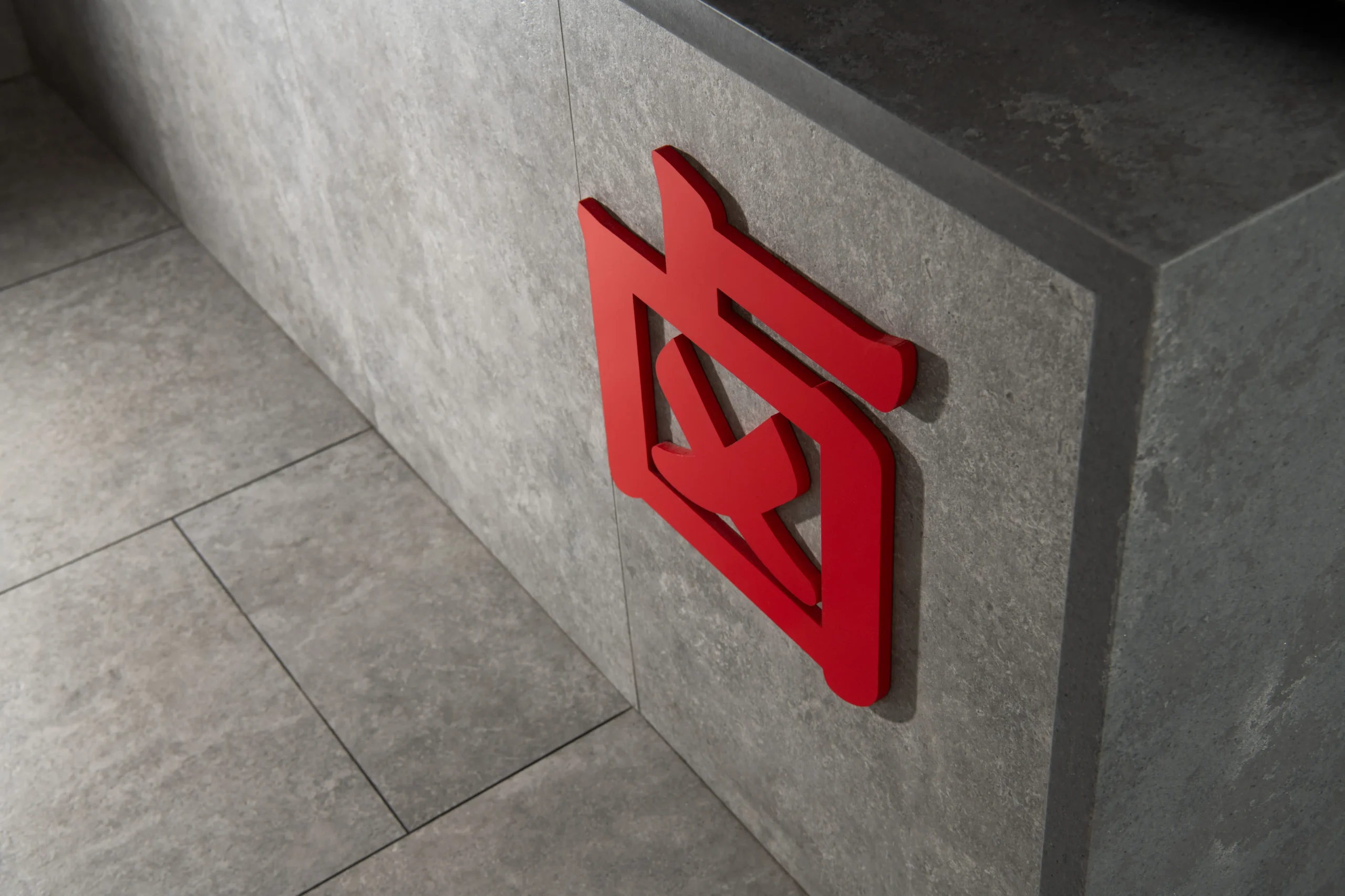 Interior Design - Red logo affixed to a gray stone wall in a modern interior setting. Dexign Matter Studio