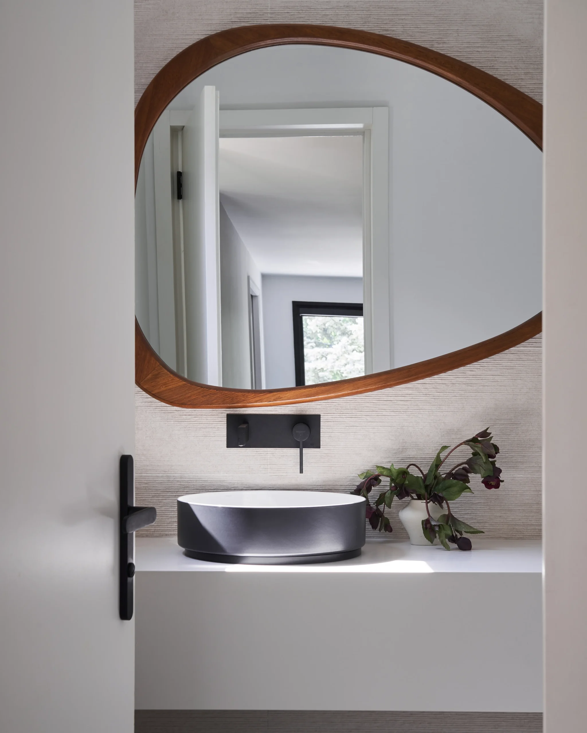 Interior Design - A modern bathroom featuring a black sink and an oval wooden mirror above it. Dexign Matter Studio