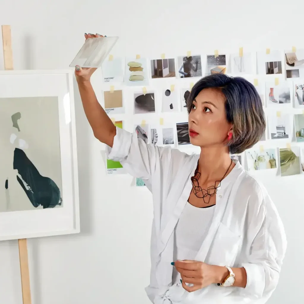 Interior Design - Guo Jingjing holding a design sample while examining artwork in a studio environment. Dexign Matter Studio