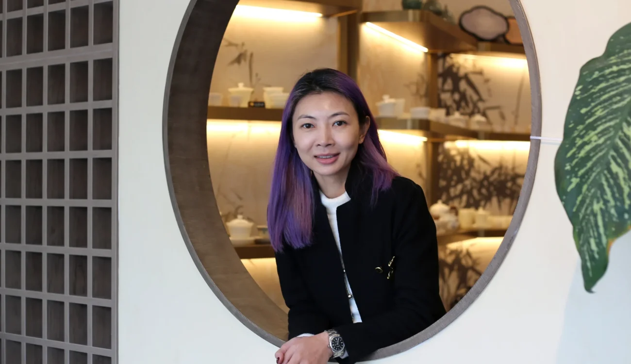 Interior Design - Portrait of Zoe-Lee with purple hair in a black blazer, leaning through a circular doorway in a modern interior with warm backlit shelves and minimalist decor. Dexign Matter Studio
