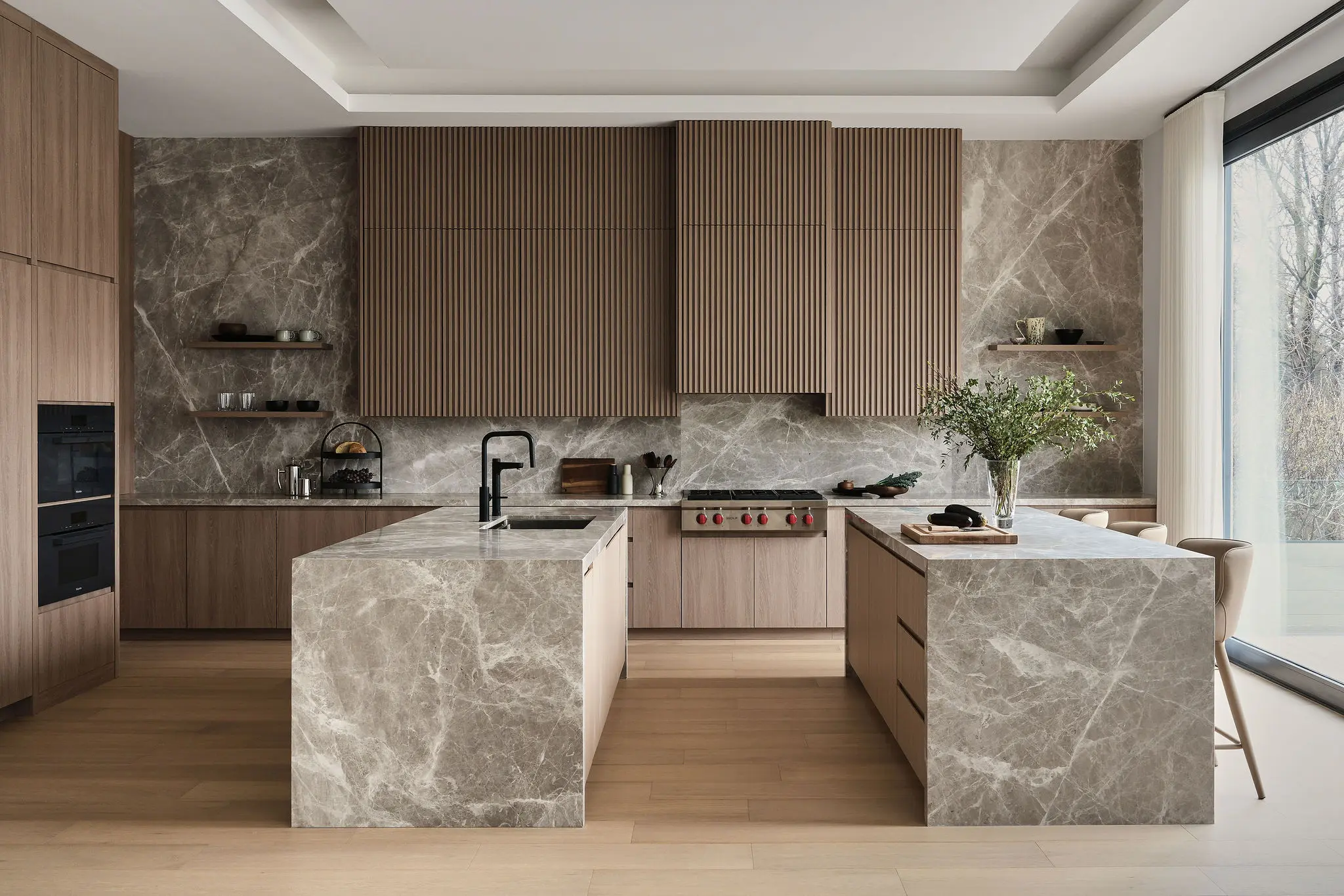 Modern kitchen with marble countertops, built-in appliances, wood cabinetry, and concealed architectural lighting behind a striped backsplash.