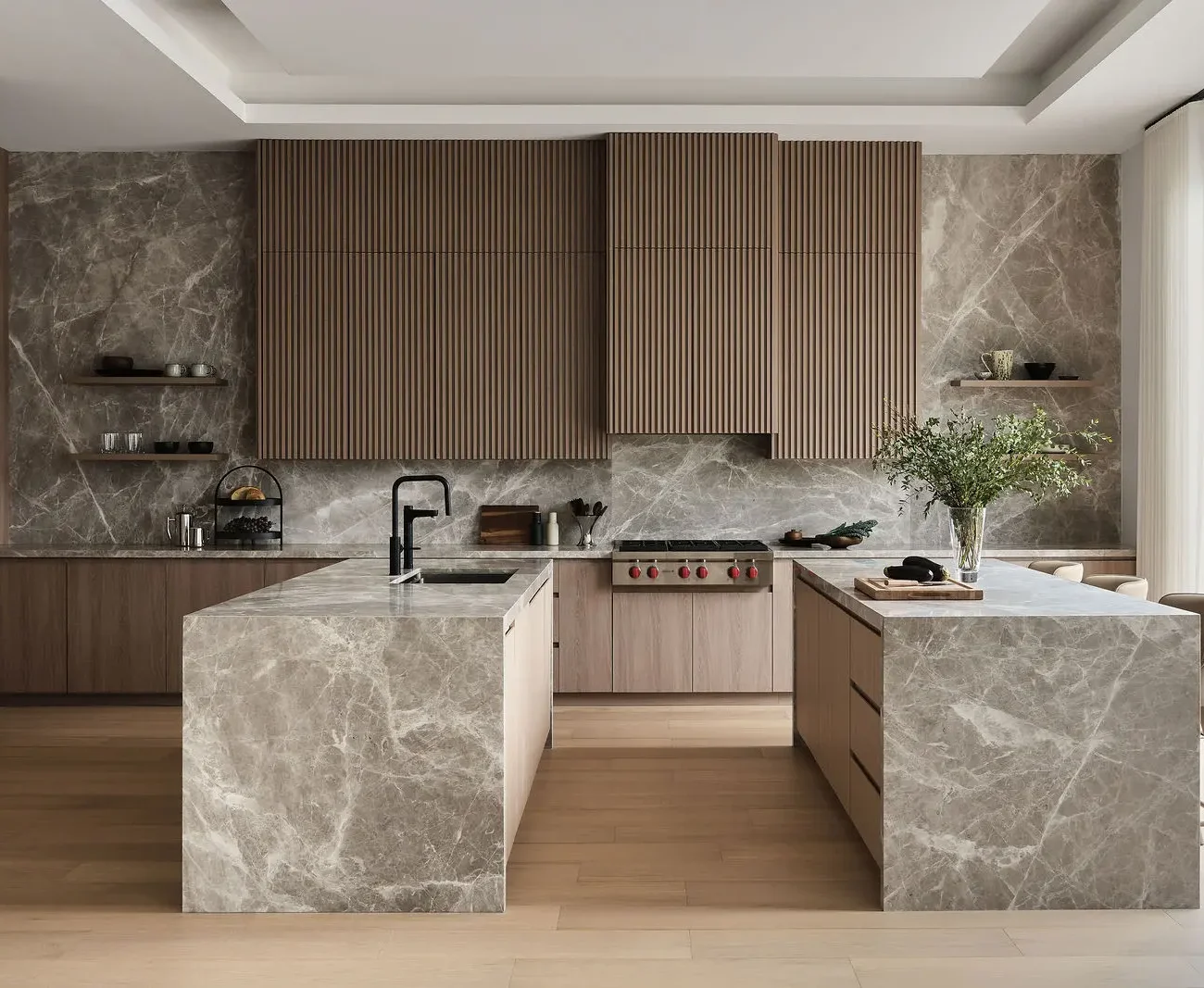 Interior Design - A contemporary kitchen combines fluted wood cabinetry, marble-clad islands, and a large window beside the dining area. Dexign Matter Studio