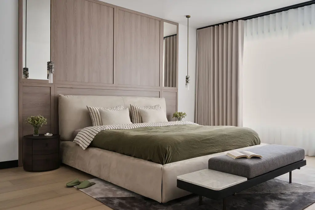 Interior Design - A serene bedroom with a beige upholstered bed, olive bedding, wood panel headboard, and soft floor-to-ceiling curtains. Dexign Matter Studio