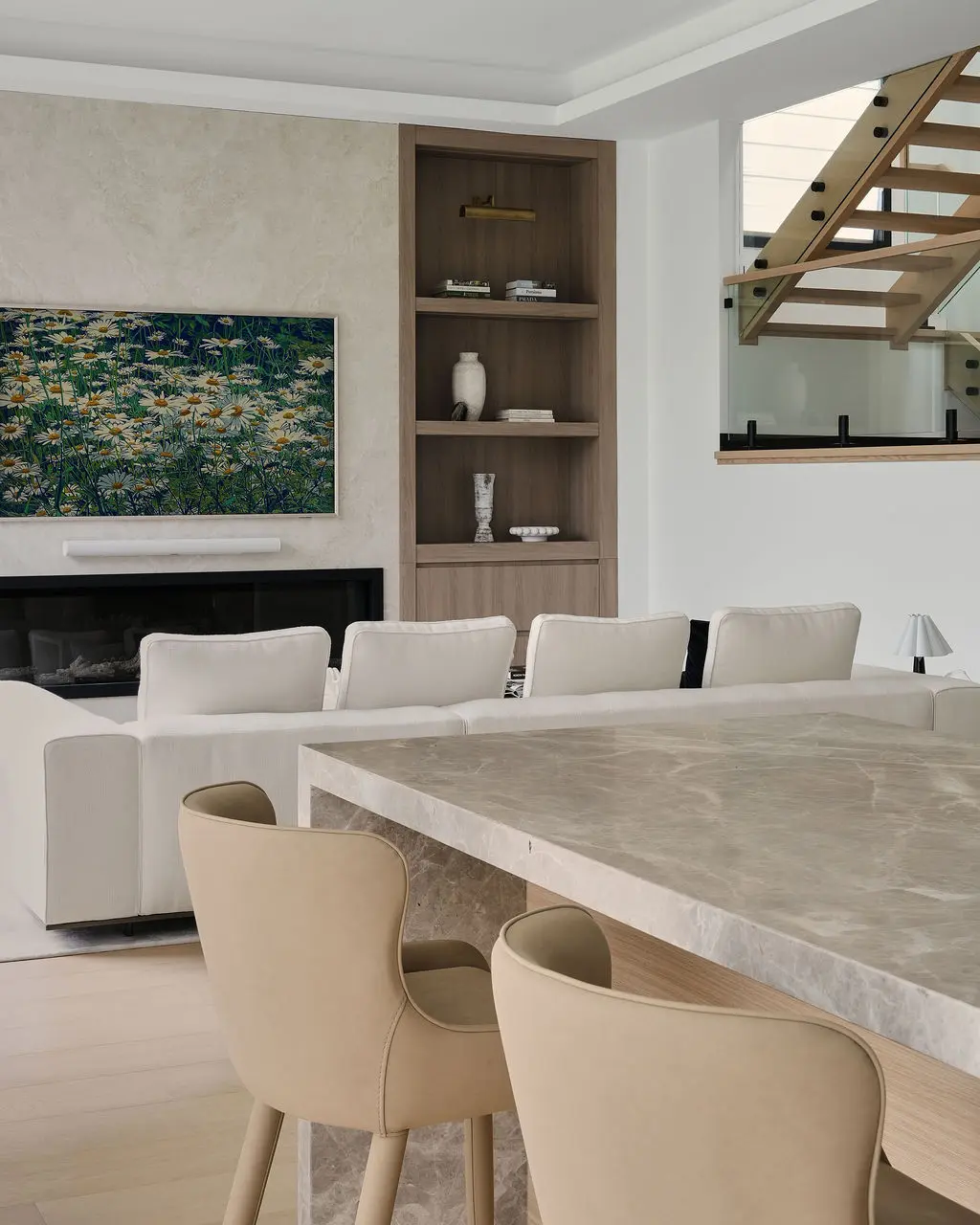 Interior Design - A modern living and dining space with a marble table, beige chairs, white sofas, and floral wall art above a fireplace. Dexign Matter Studio