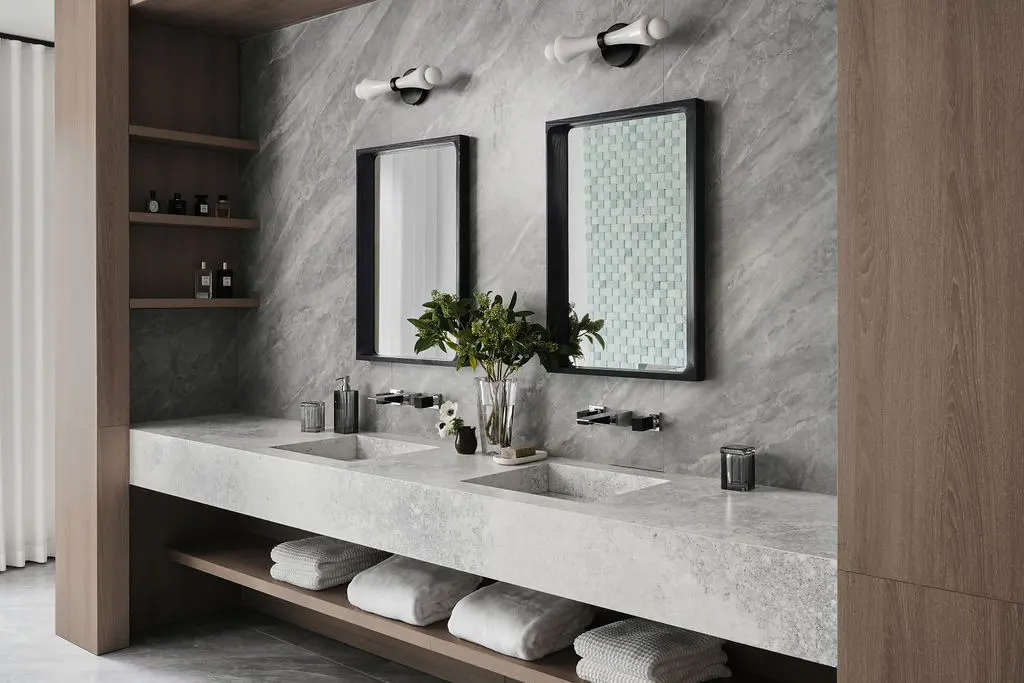 Interior Design - A modern double vanity bathroom with gray marble walls, twin black-framed mirrors, wood cabinets, and green plants. Dexign Matter Studio