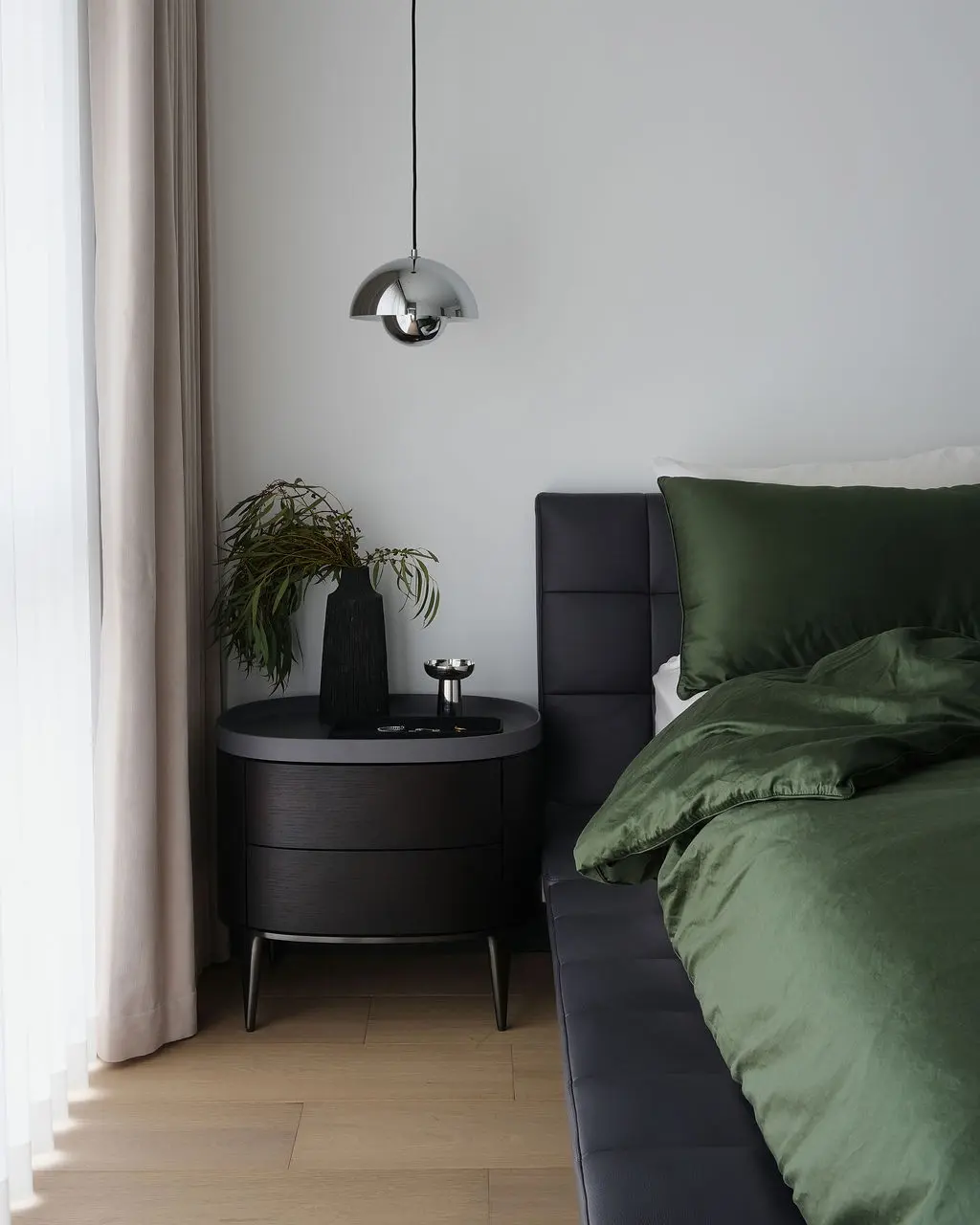 Interior Design - A modern bedroom corner shows green bedding, a black bedside table with a plant, and a chrome pendant lamp. Dexign Matter Studio