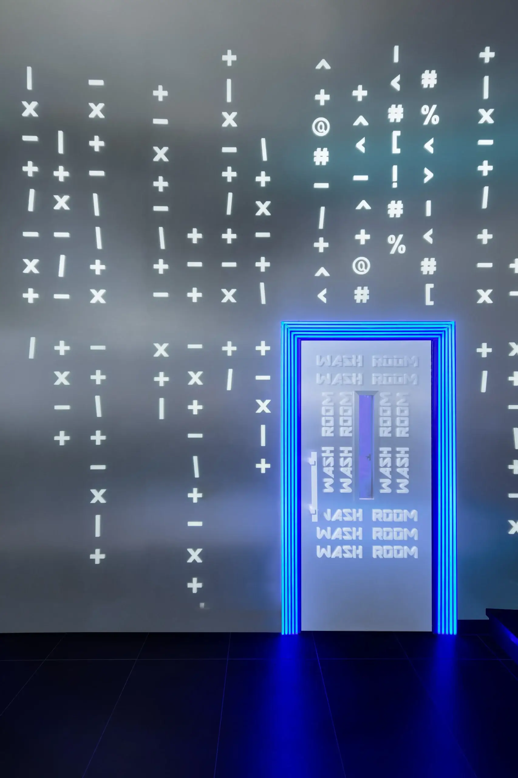 A futuristic scene featuring a doorway outlined by bright blue neon frames. The surrounding wall is lit with white symbols and characters, creating a grid of alphanumeric shapes, while the door area repeats the words 'WASH ROOM' in a vertical pattern.